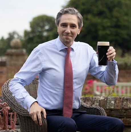 Simon Harris sits on a wicker chair as though it is made of thumbtacks and holds up a pint cc Number 10